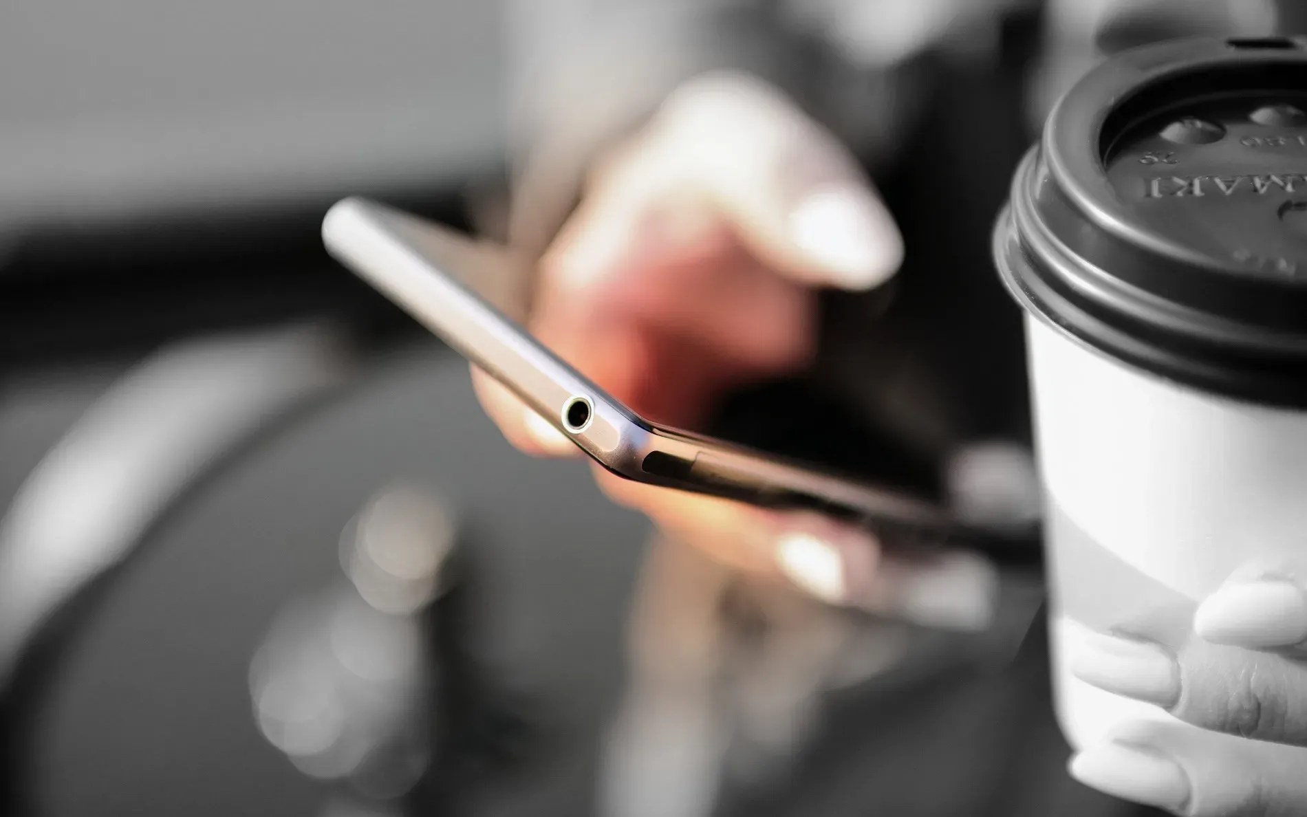 Person holding a smartphone and a takeaway coffee cup