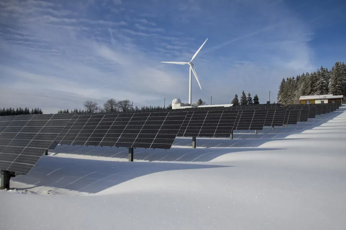 Solar panel rows in a snow-covered field with a wind turbine behind them